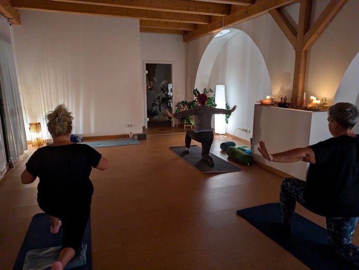Yoga-Gruppe im Ausfallschritt, die Arme weit geöffnet, im warmen Licht des Studios